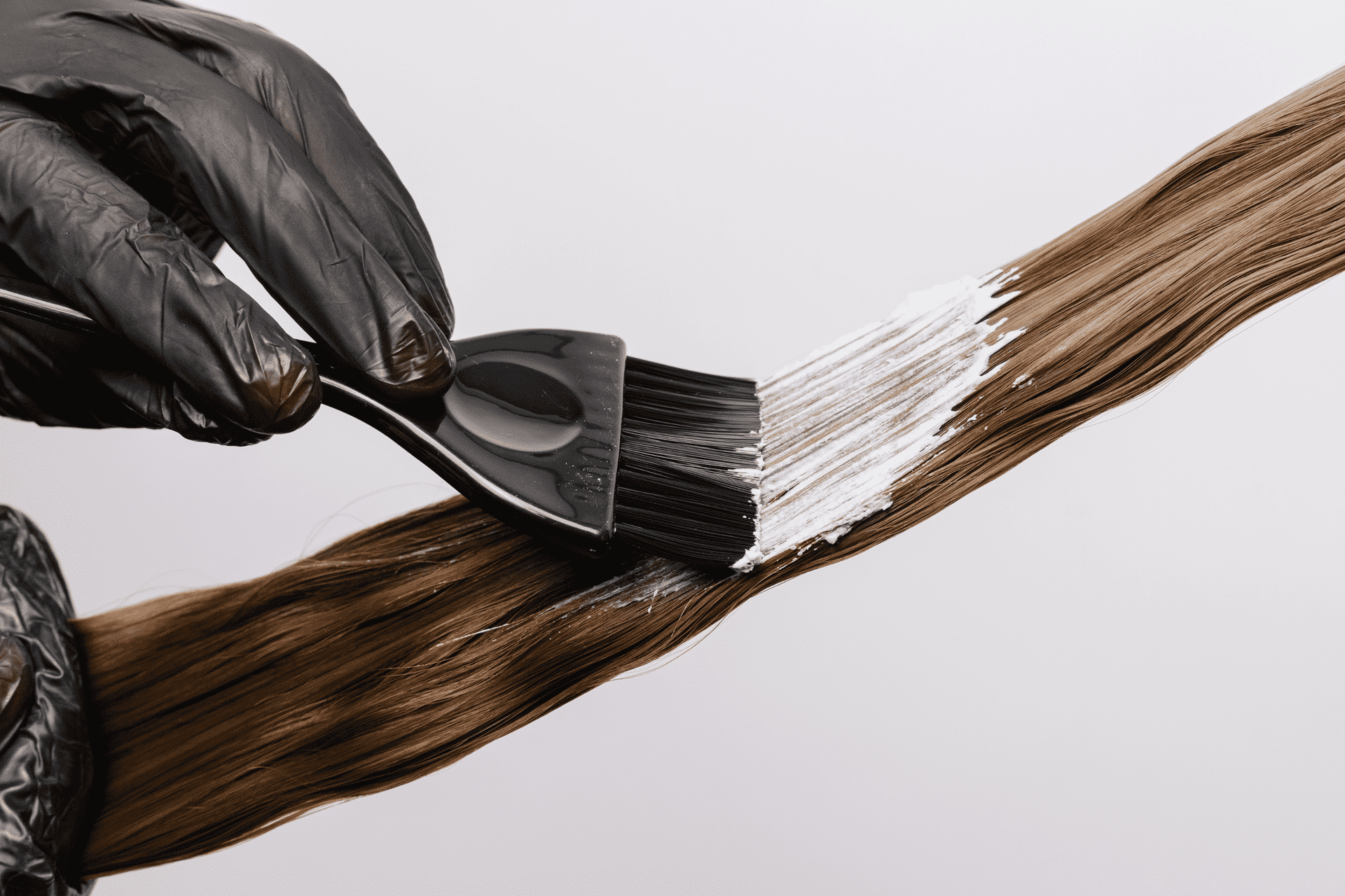 Hair coloring process: hand applying dye to brown hair with brush and black gloves.