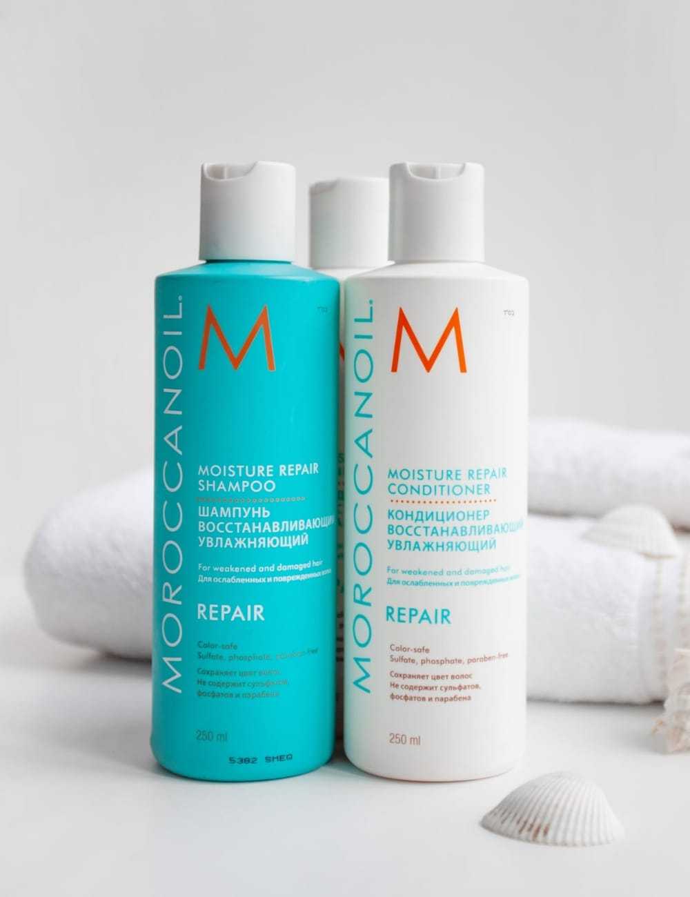Moroccanoil Moisture Repair Shampoo and Conditioner bottles on white towels with sea shells.