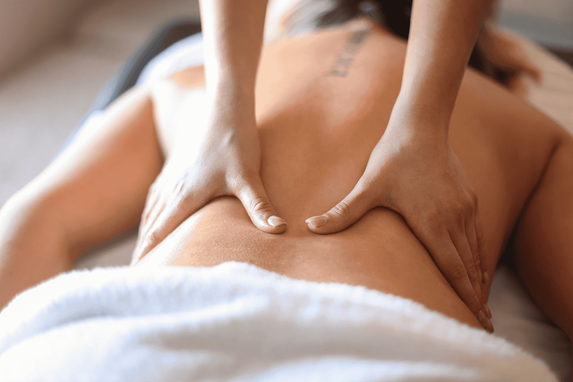 Person receiving a back massage with therapist focusing on the lower back muscles.