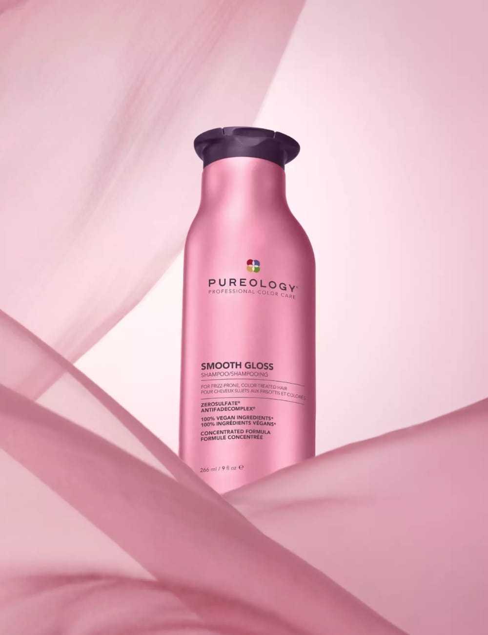 Pink Pureology shampoo bottle on a pink background, surrounded by flowing pink fabric.