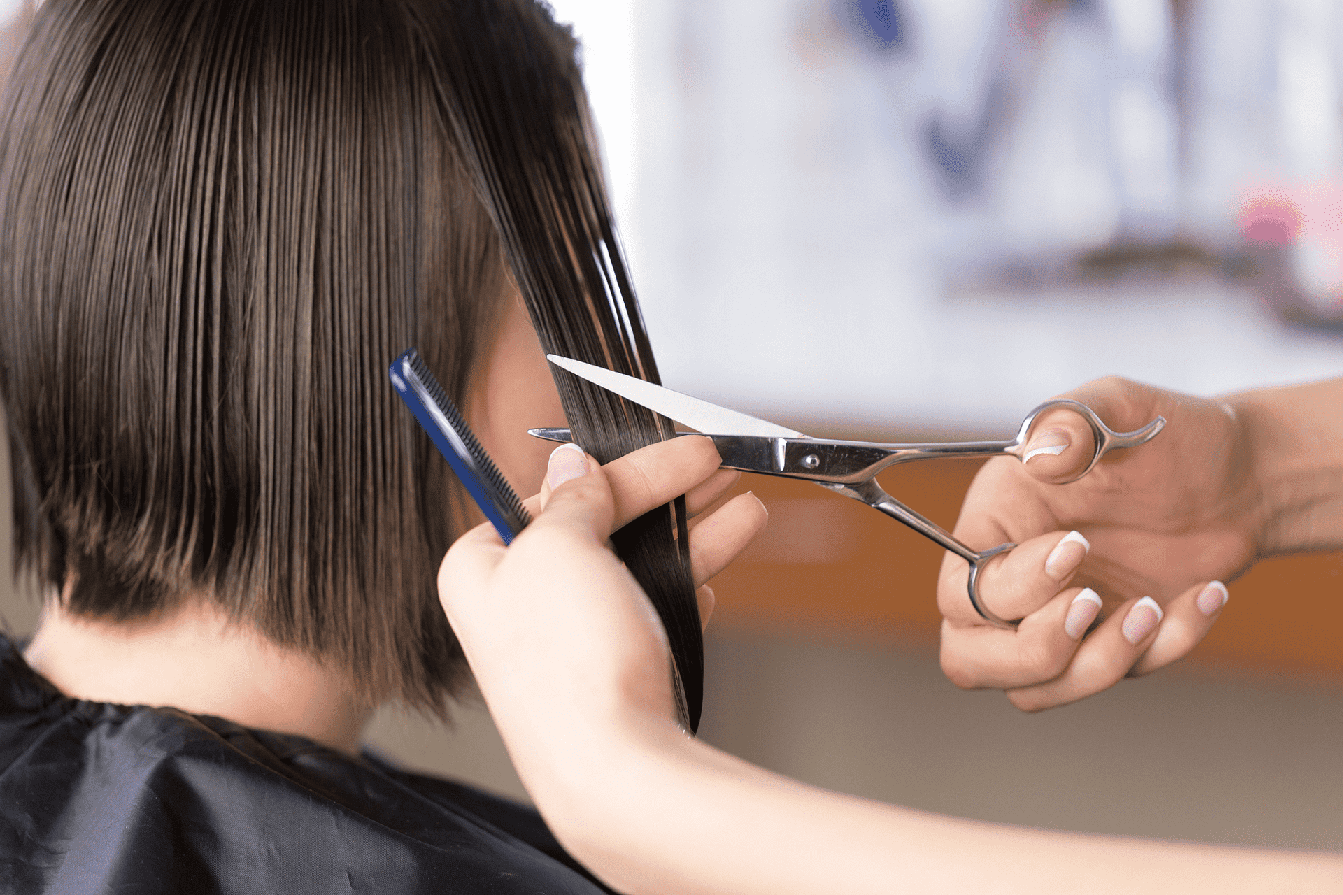 A close-up of a person getting a haircut with scissors and a comb in a salon.