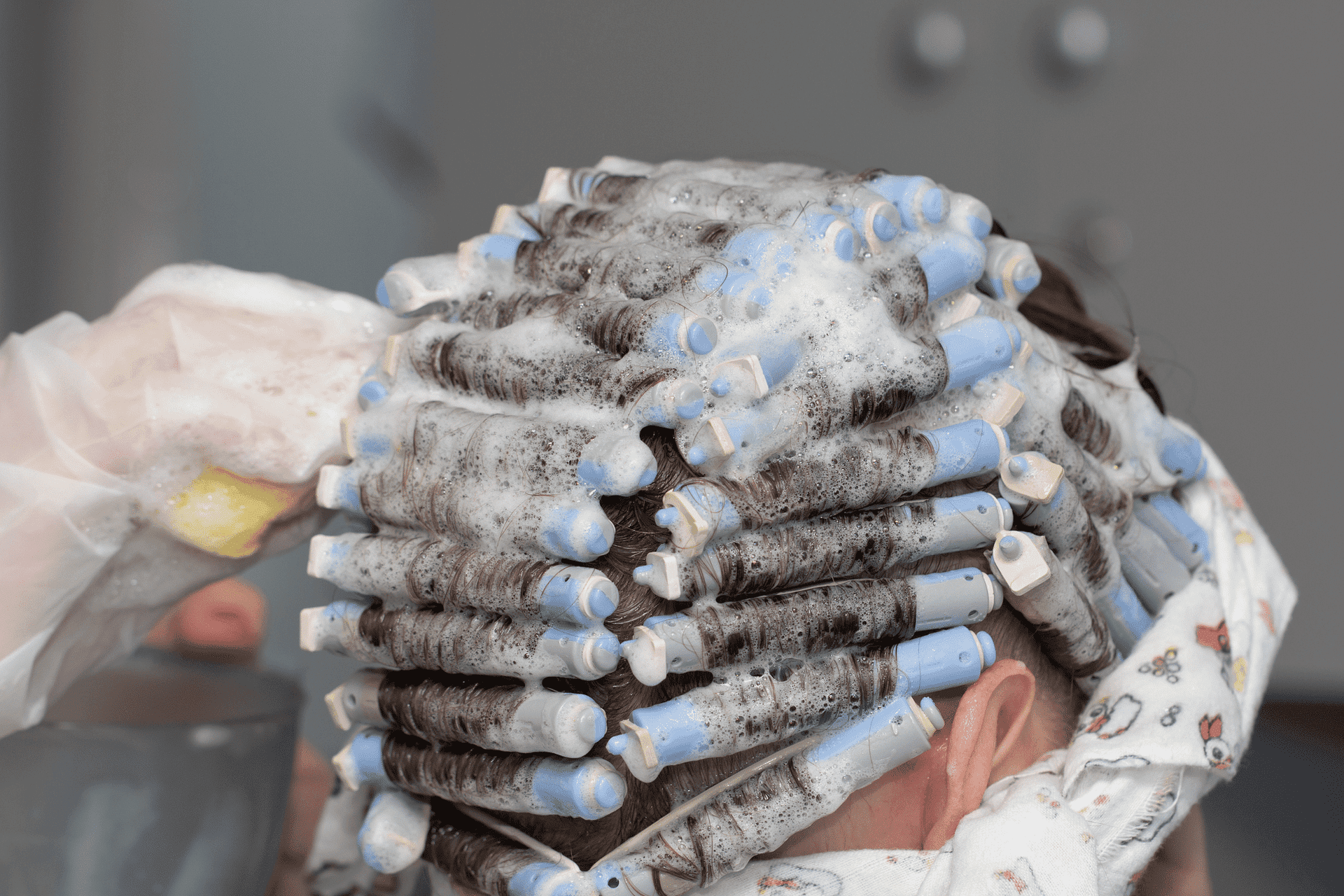 Person getting a perm with blue rods and foam in a salon.