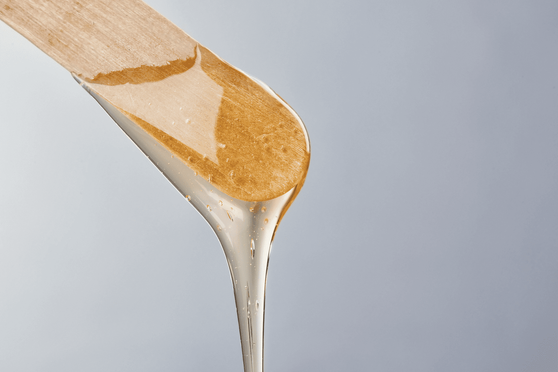 Wooden applicator with honey-colored wax, ready for use, against a light grey background.